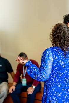 A woman in a blue dress leads a group discussion indoors, focusing attention on diverse individuals.