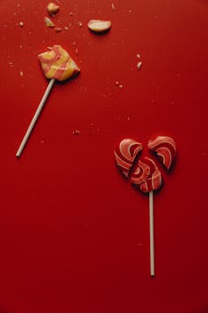Two heart-shaped lollipops on a red backdrop, one broken symbolizing love.